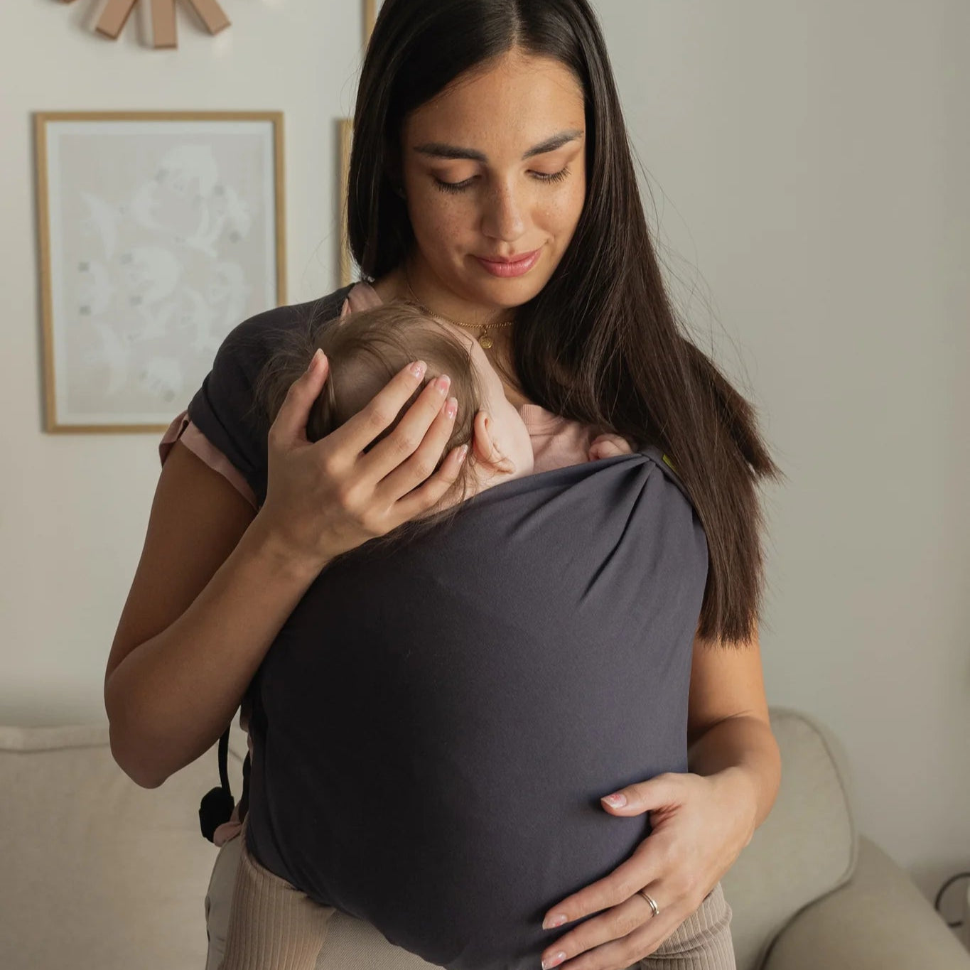 Woman holding a baby in a carrier in a cozy living room.