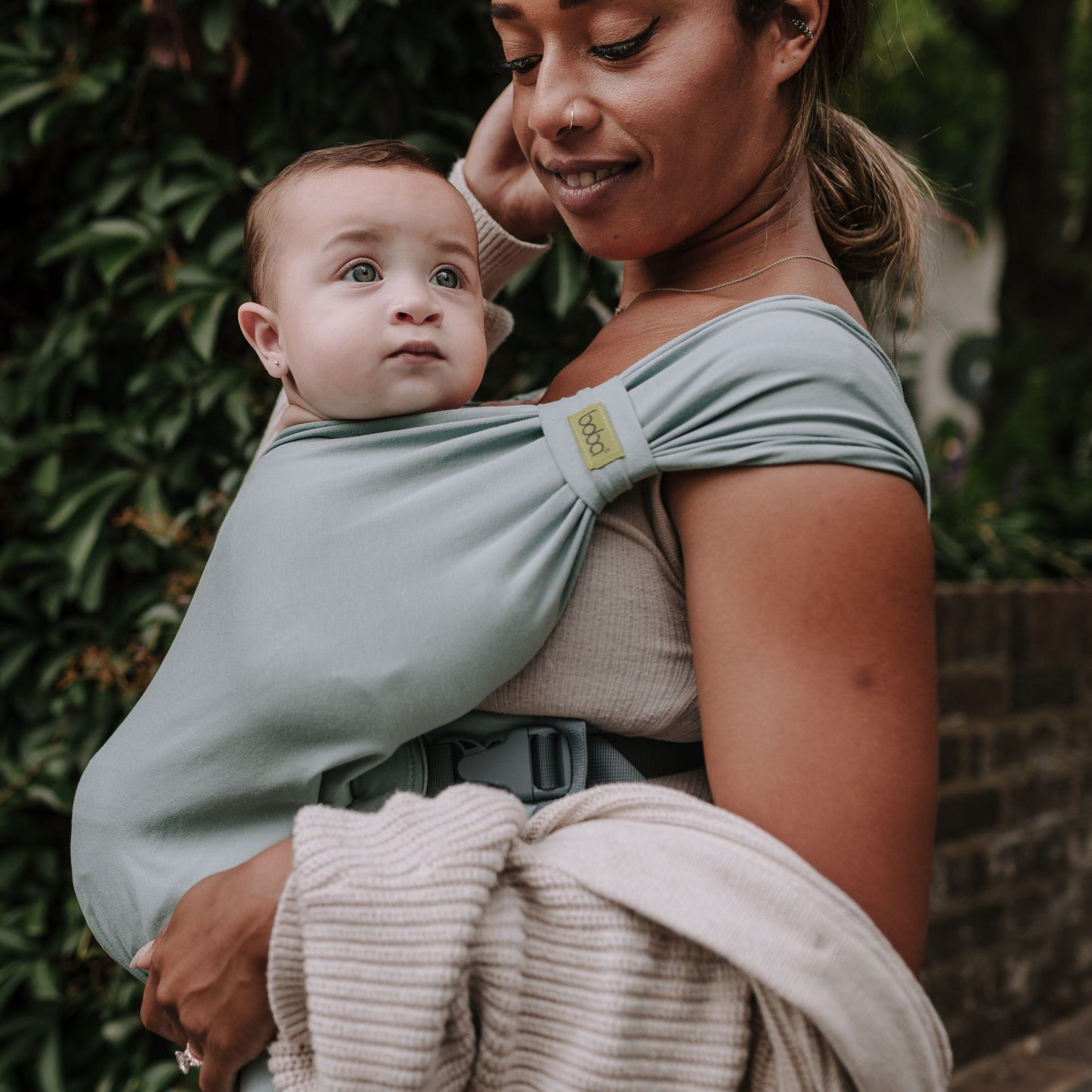 Woman holding a baby in a sling against a green leafy background