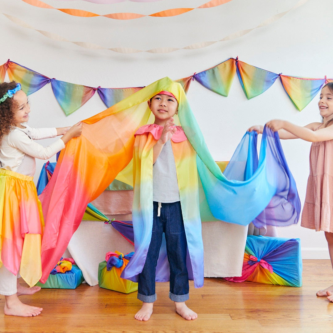 Children playing with rainbow fabric in a room decorated with rainbow flags.