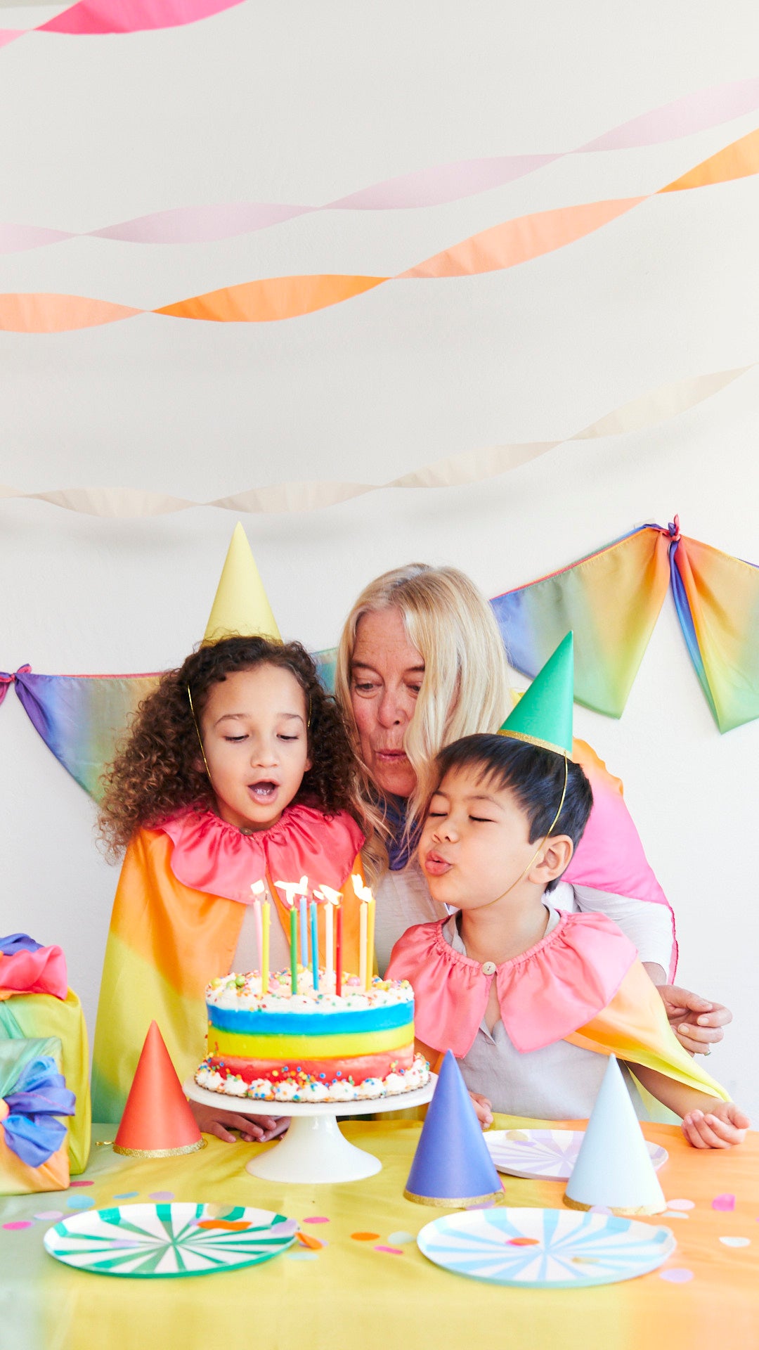 Children and a woman celebrating a birthday with a cake and candles at a table.