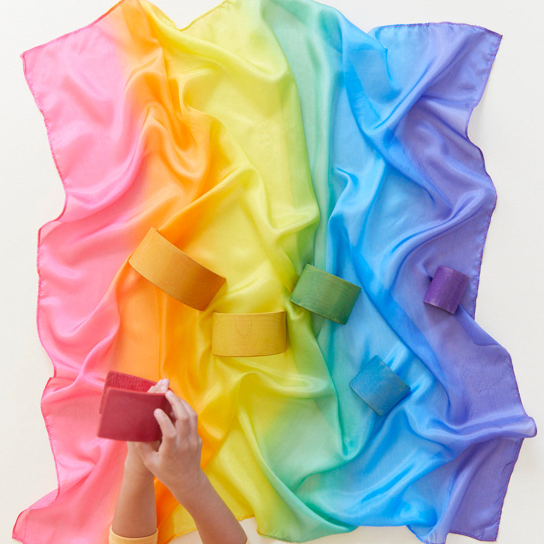 Colourful rainbow silk with wooden toys on a white background