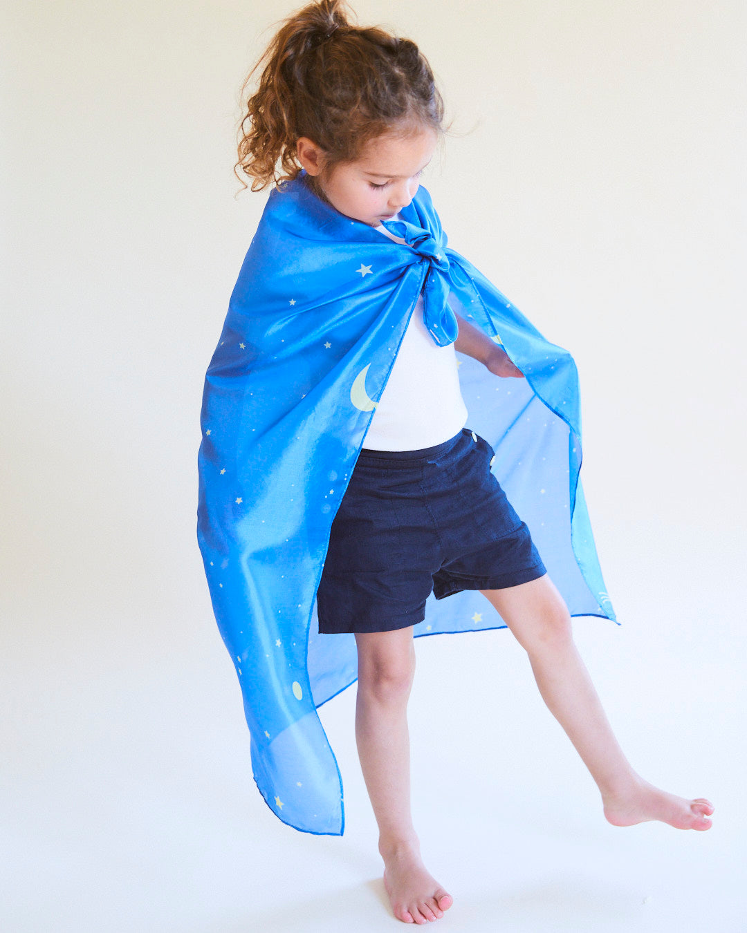 Child wearing a blue cape with star and moon designs on a white background