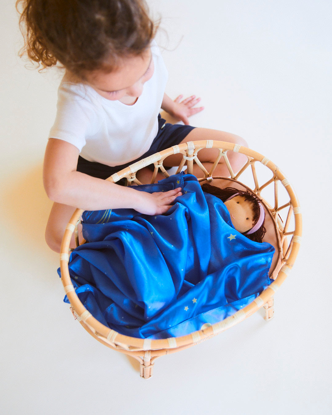 Child playing with a doll in a wicker basket on a light background
