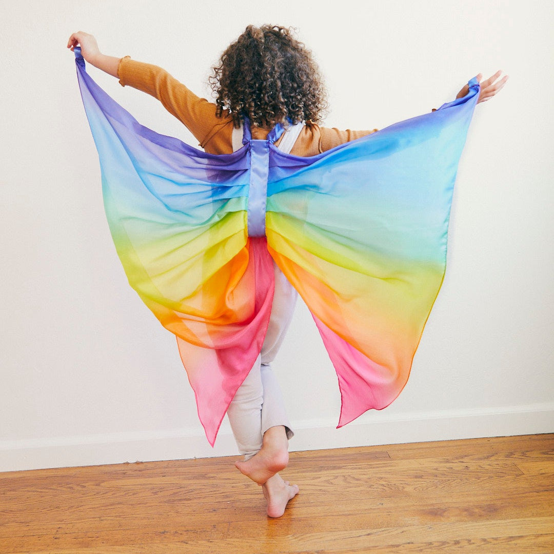 Person wearing a colourful butterfly costume on a wooden floor with a white wall background