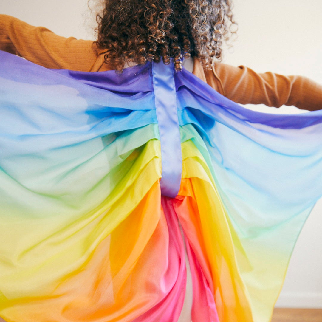 Person wearing a rainbow dreass-up wings with a plain background