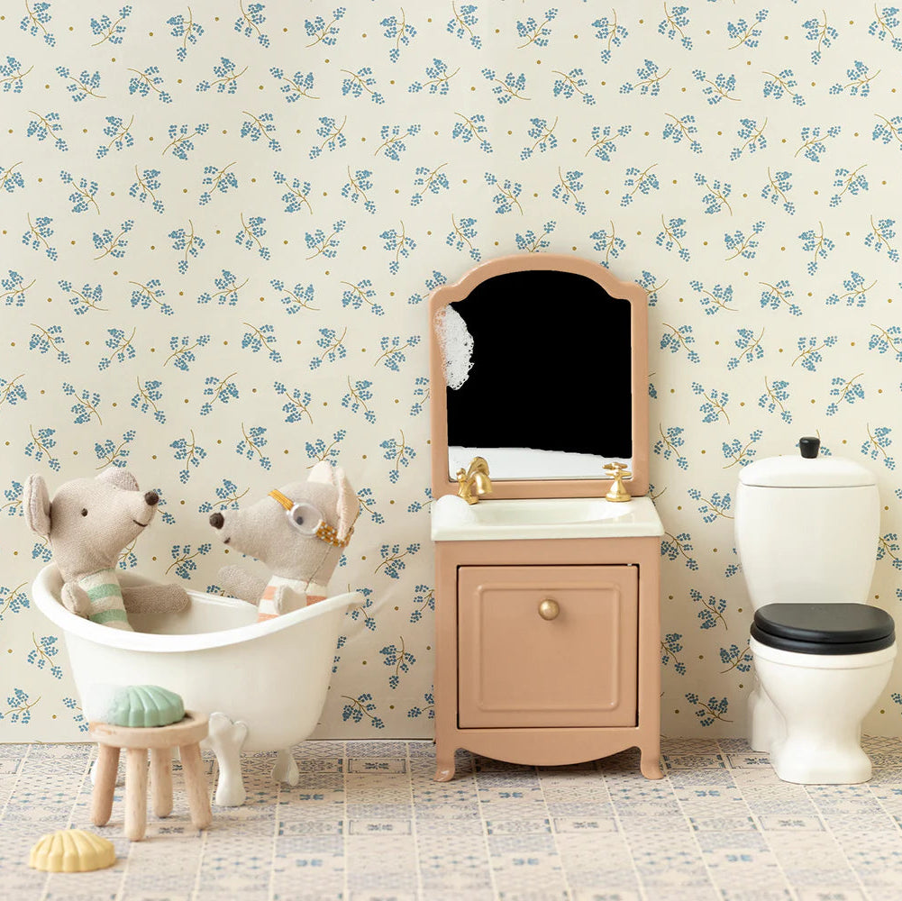Bathroom setting with a vanity, toilet, and decorative wall paper.