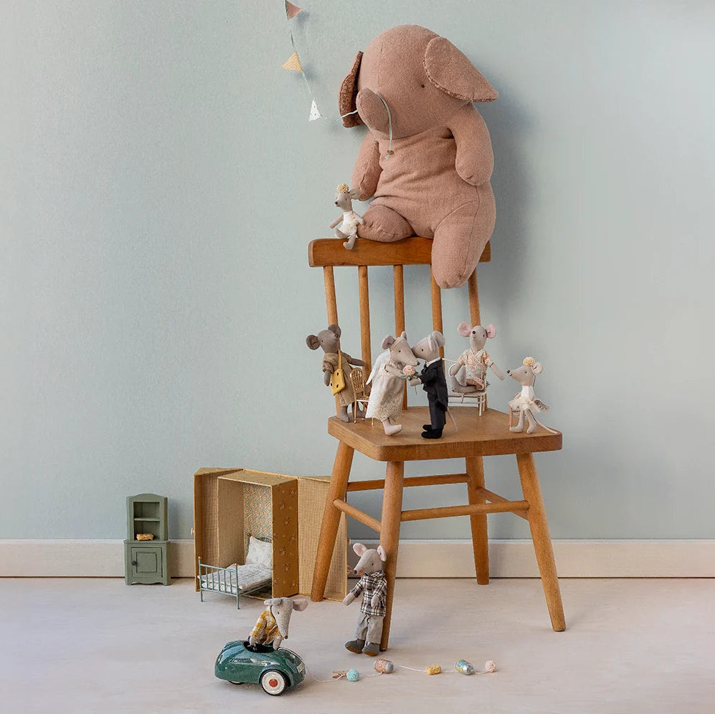 Children's toys including a plush elephant and teddy bears on a wooden stool against a light blue wall.