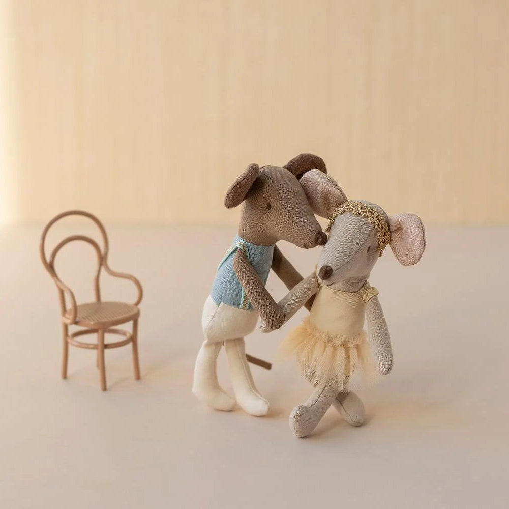 Two toy mice in ballet costumes standing next to a small chair on a light background