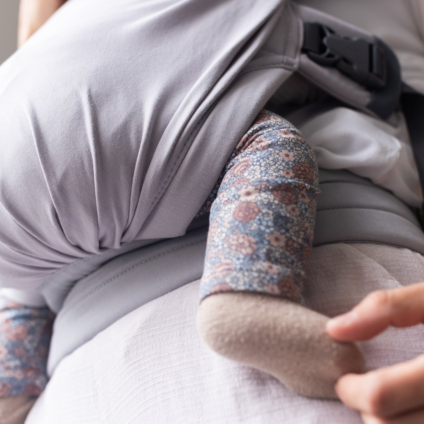 Person using a baby carrier with a baby inside, focusing on the carrier and baby's arm.
