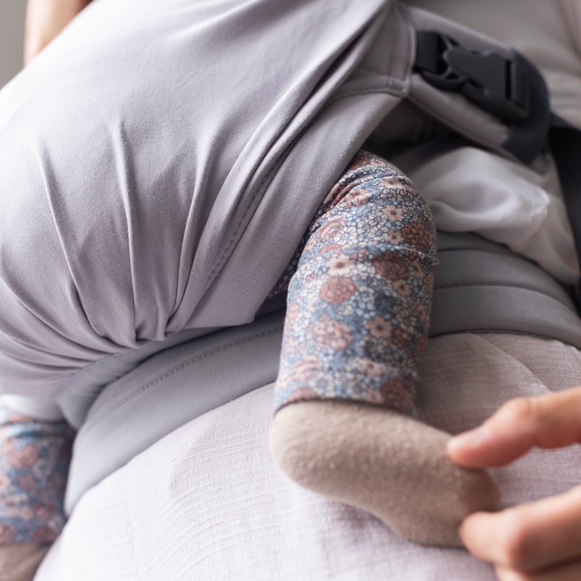 Person using a baby carrier with a baby inside, focusing on the carrier and baby's arm.