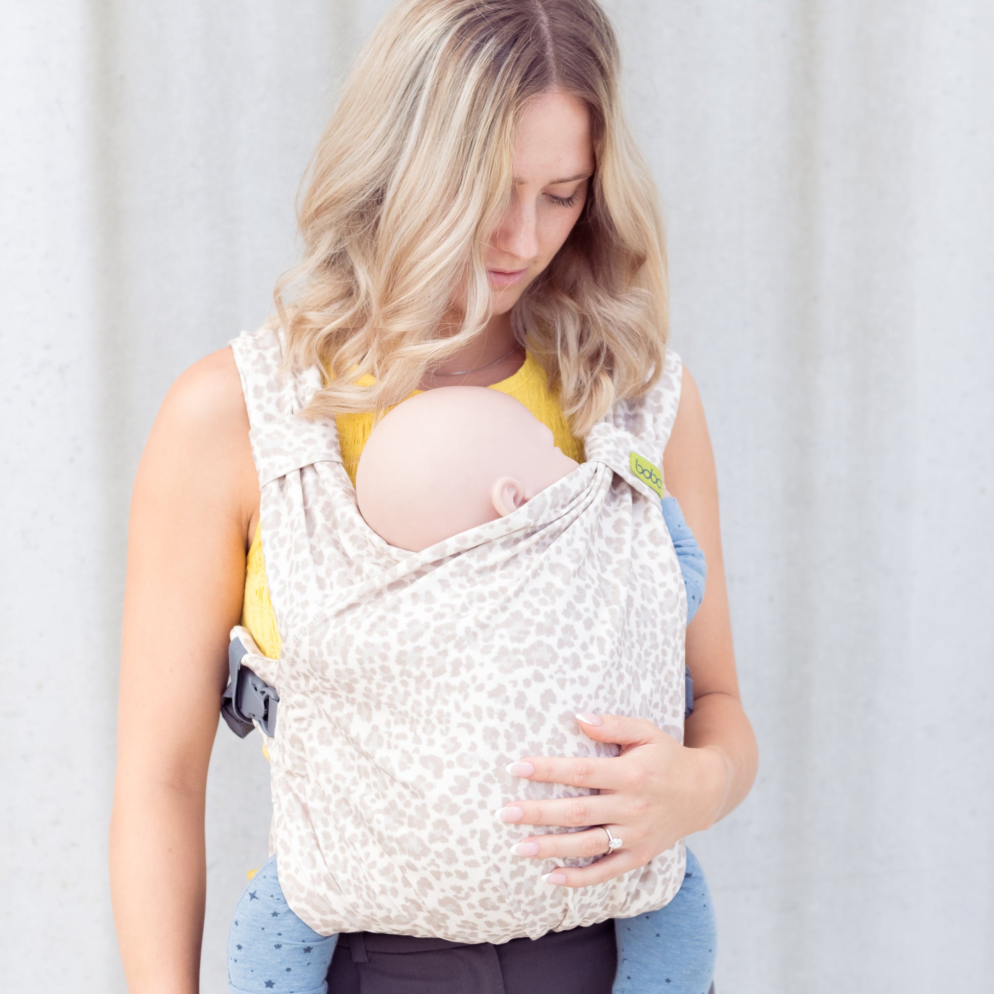 Woman holding a baby in a carrier against a plain background
