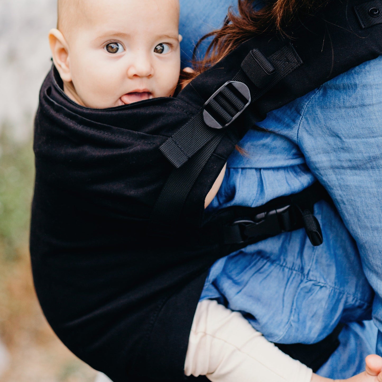 Baby in a black carrier held by a person outdoors