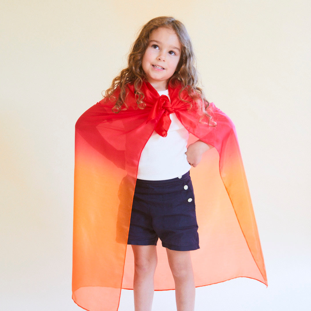 Child wearing a red and orange superhero cape on a plain background