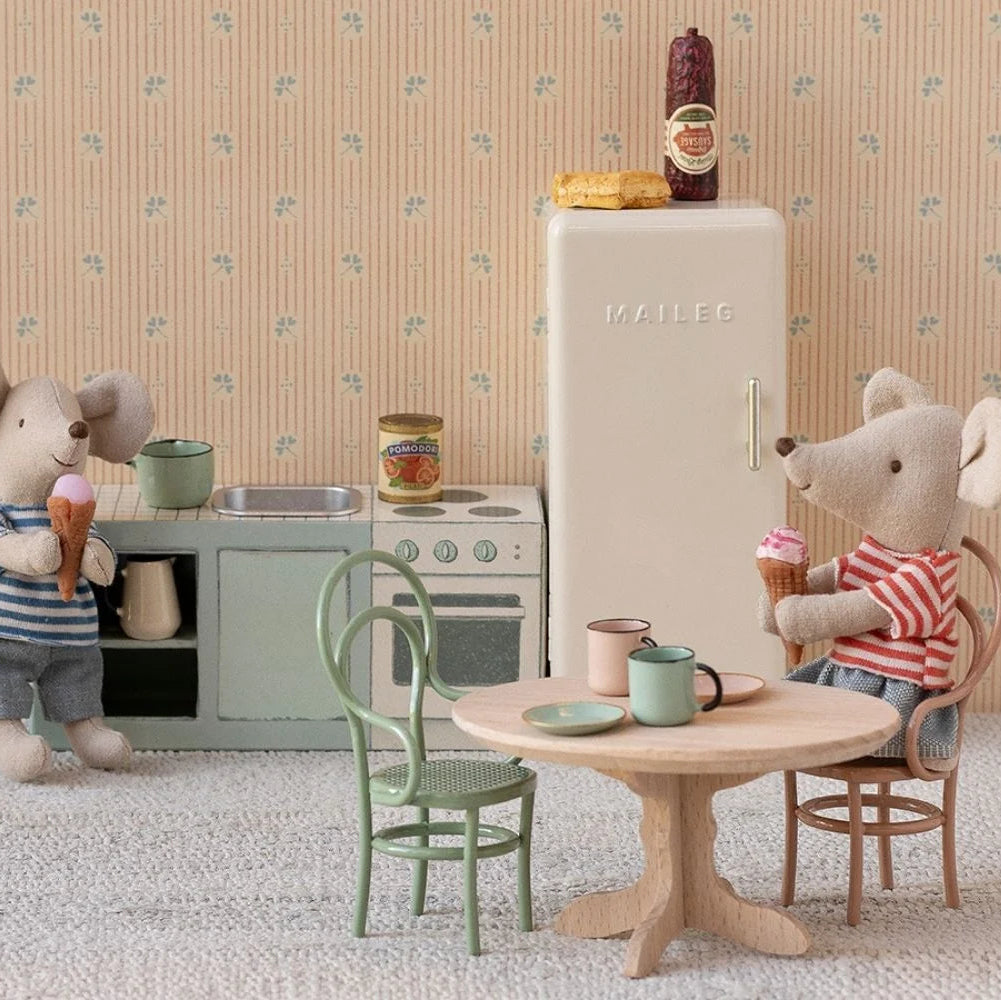 Miniature kitchen scene with toy mice, refrigerator, and furniture against a patterned wall.