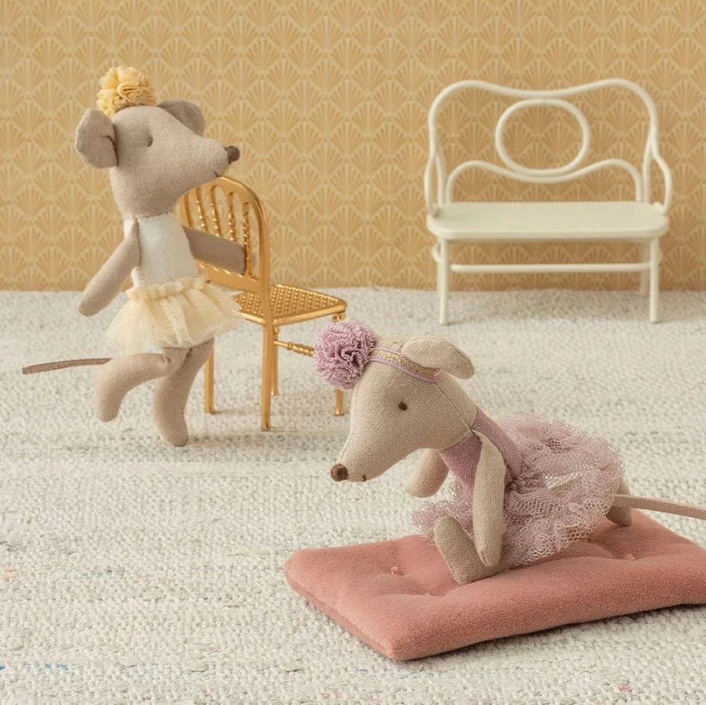 Two toy mice in decorative outfits on a textured surface with chairs in the background.