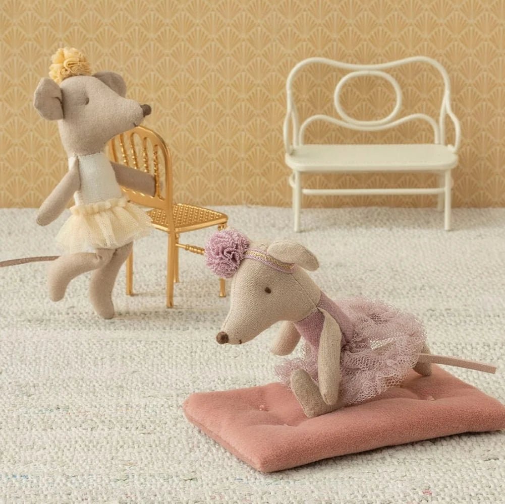 Two toy mice in decorative outfits on a textured surface with chairs in the background.