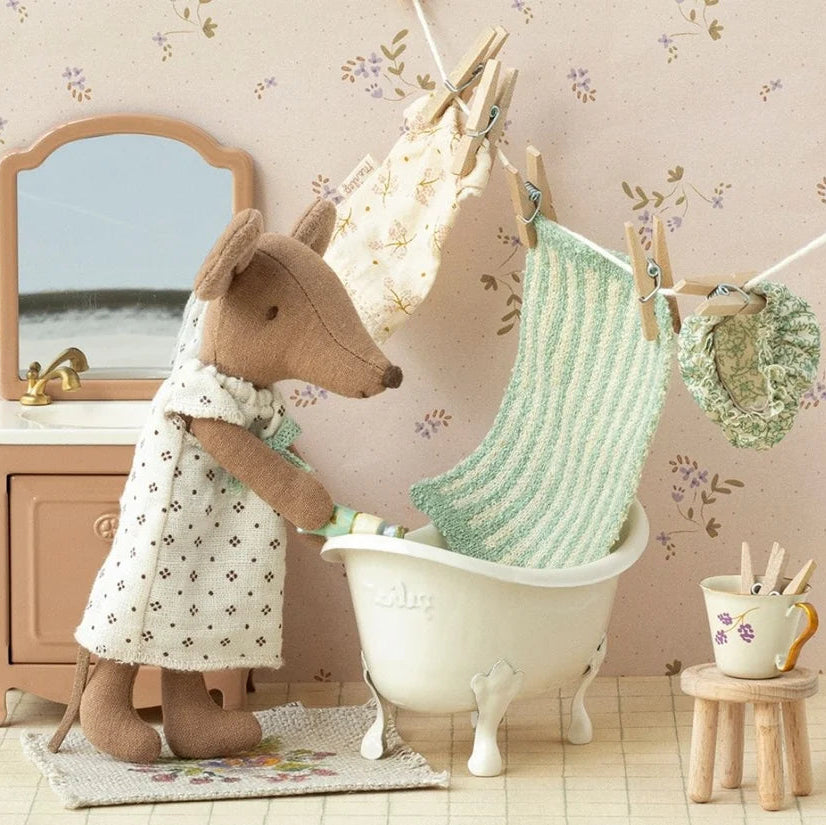 Stuffed animal in a bathroom setting with a bathtub and clothesline.