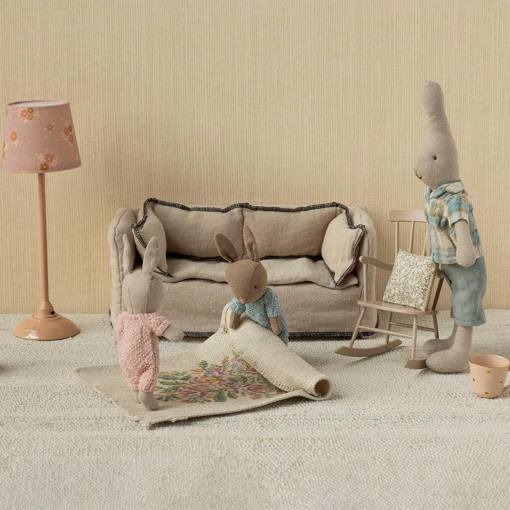 Children's room with toy sofa, rabbit figure, and lamp against a beige wall.