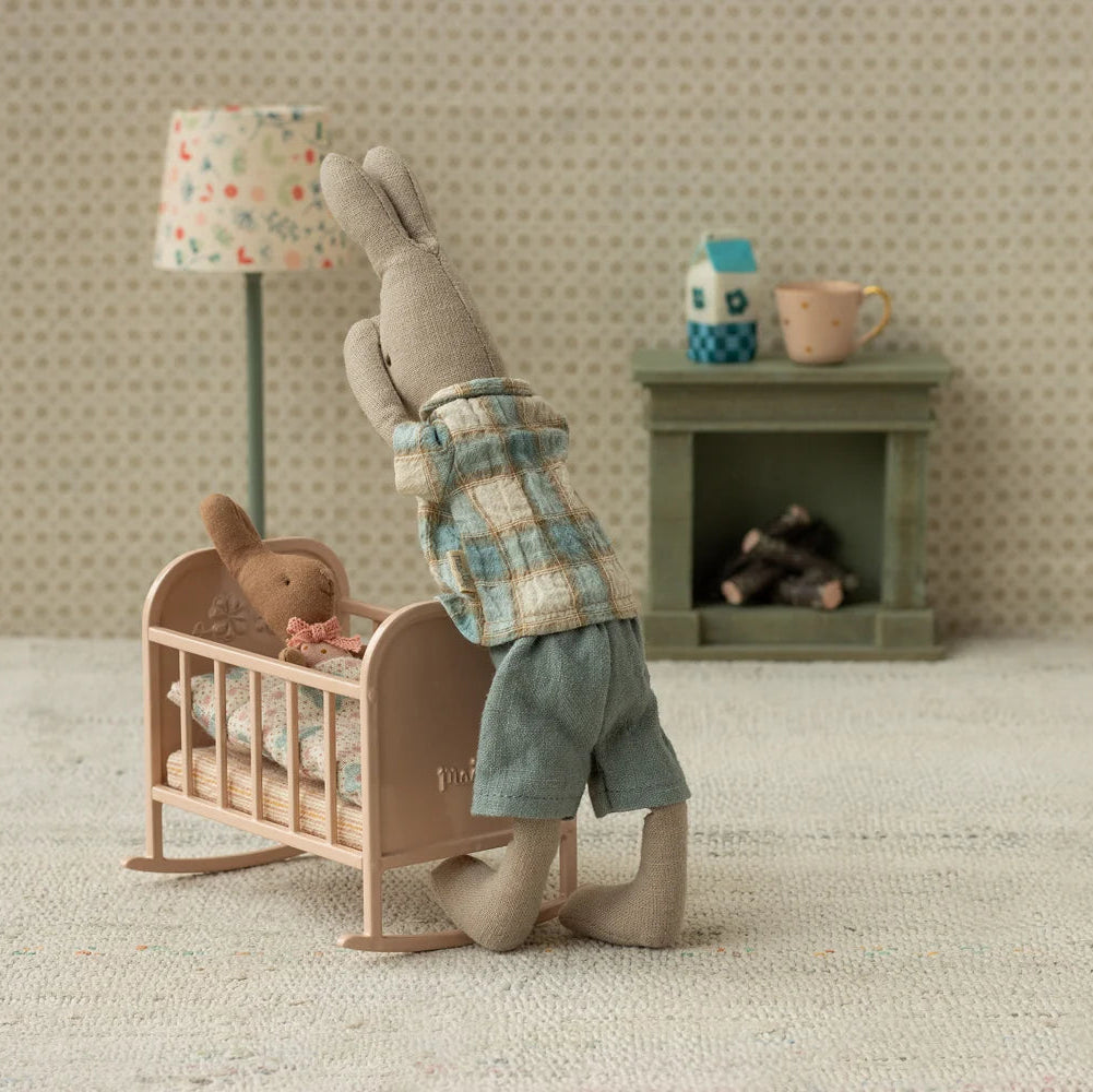 Miniature scene with a rabbit standing next to a baby crib in a cozy room.