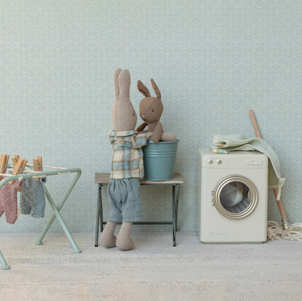 Children's room with stuffed animals, washing machine, and laundry basket against a light blue wall.