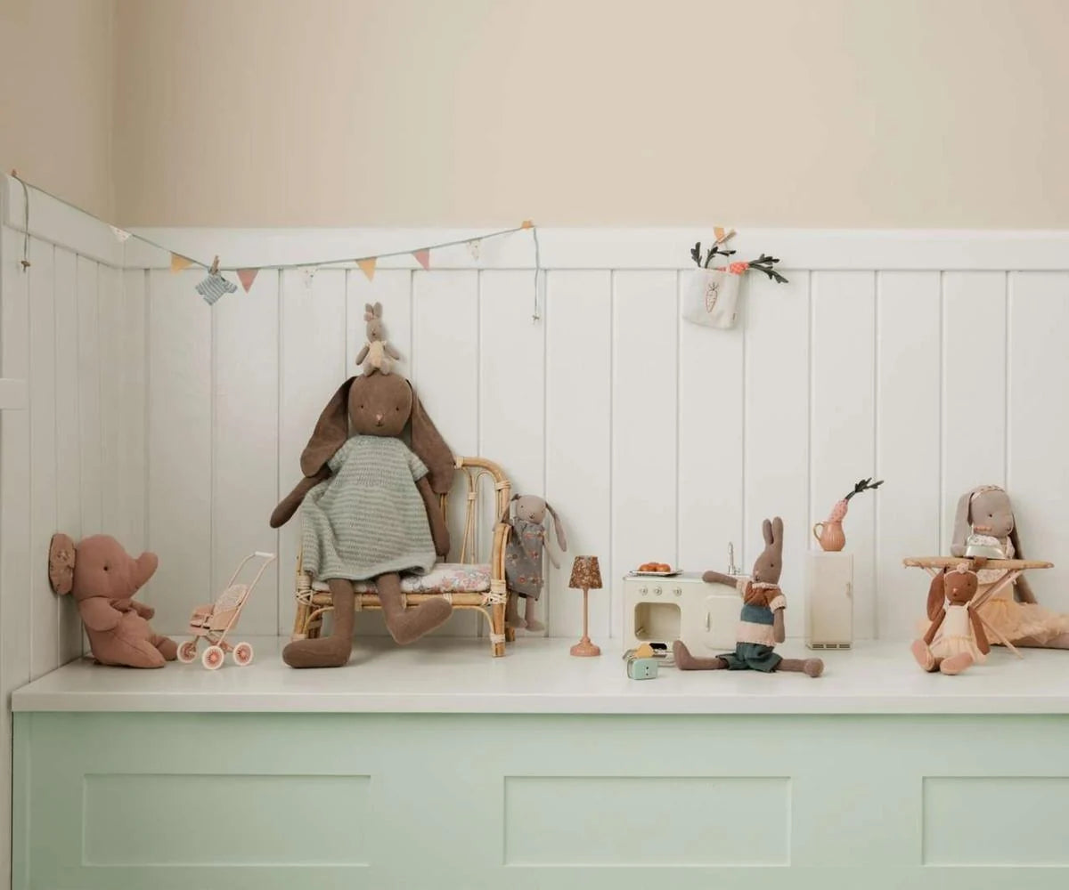 Children's toys including a rabbit, elephant, and other plush figures on a white shelf against a beige wall.