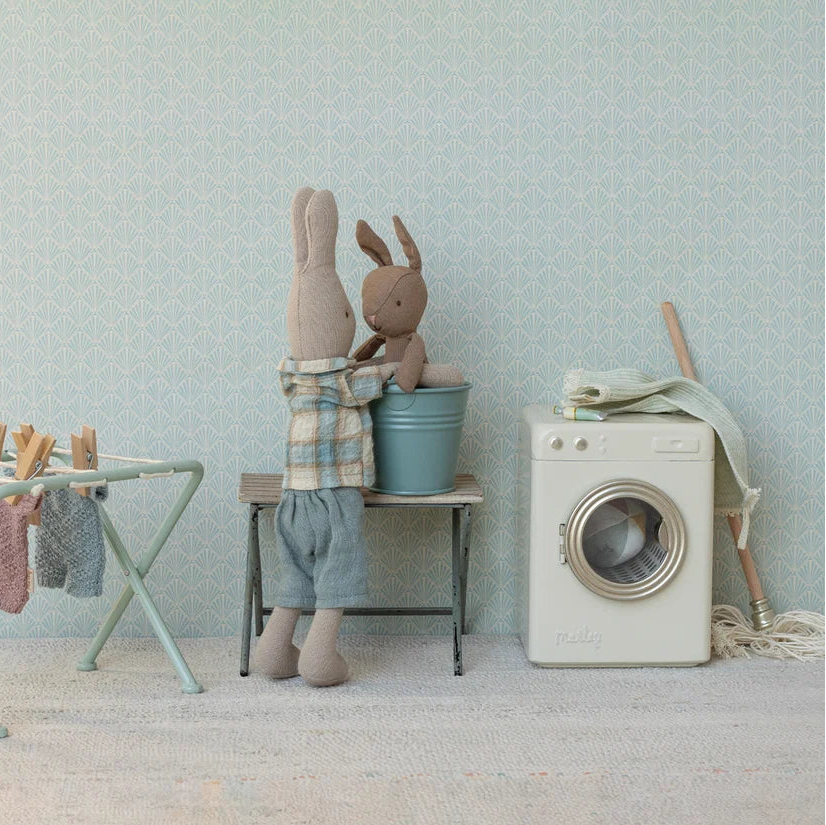 Stuffed animals with washing machine, and laundry basket against a light blue wall.