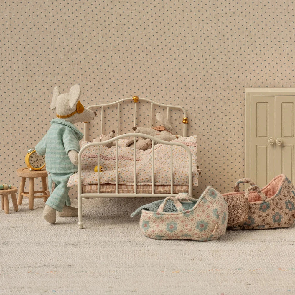 Miniature bedroom scene with a child's bed, toys, and furniture against a polka dot wall.