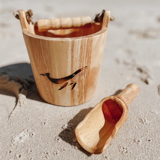 Wooden bucket and scoop on a sandy beach with ocean in the background